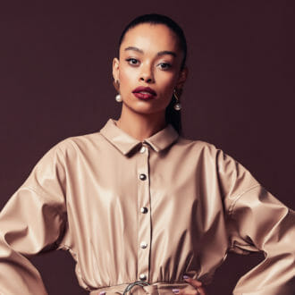 Woman posing in a jumpsuit with earrings on a brown background.