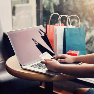 Person online shopping with credit card with bags of merchandise next to them.