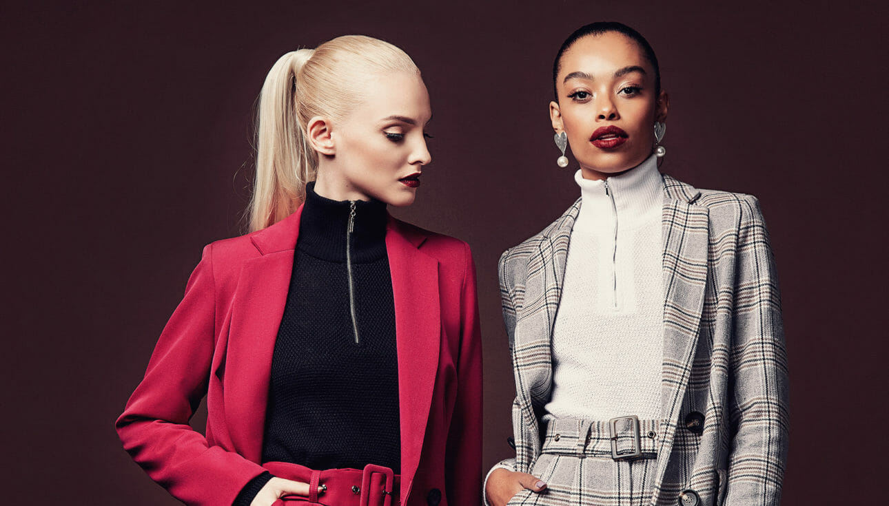 A fashion image of two women posing in blazers on a brown background.