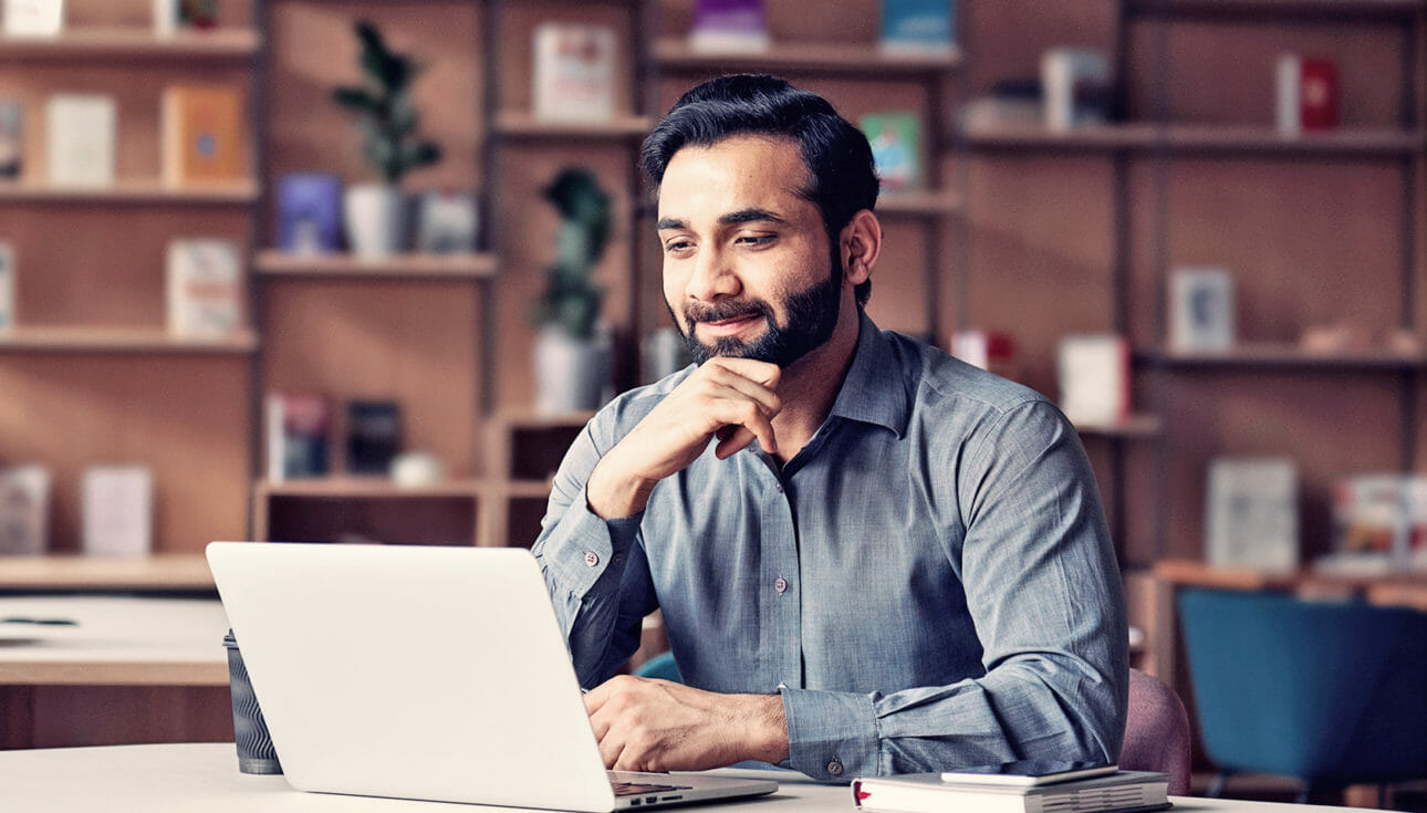 Man in a collared shirt smiling at his laptop while he is online shopping for fashion retail products.