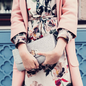 Fashion model in a fancy dress holding a purse near a blue geometric wall.