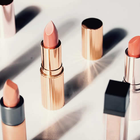 Beauty product: Gold tubes of lipstick standing up on a table with sunshine on them.