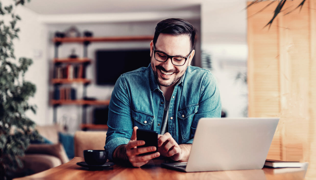 Man with glasses smiling at his phone while searching a retail site for products.