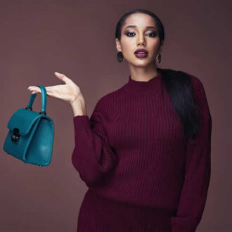 Fashion model holding a teal purse while posing in a maroon sweater.