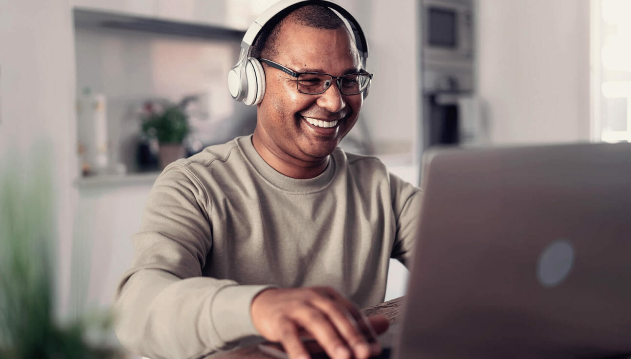 A man smiling at his laptop as he online shops.