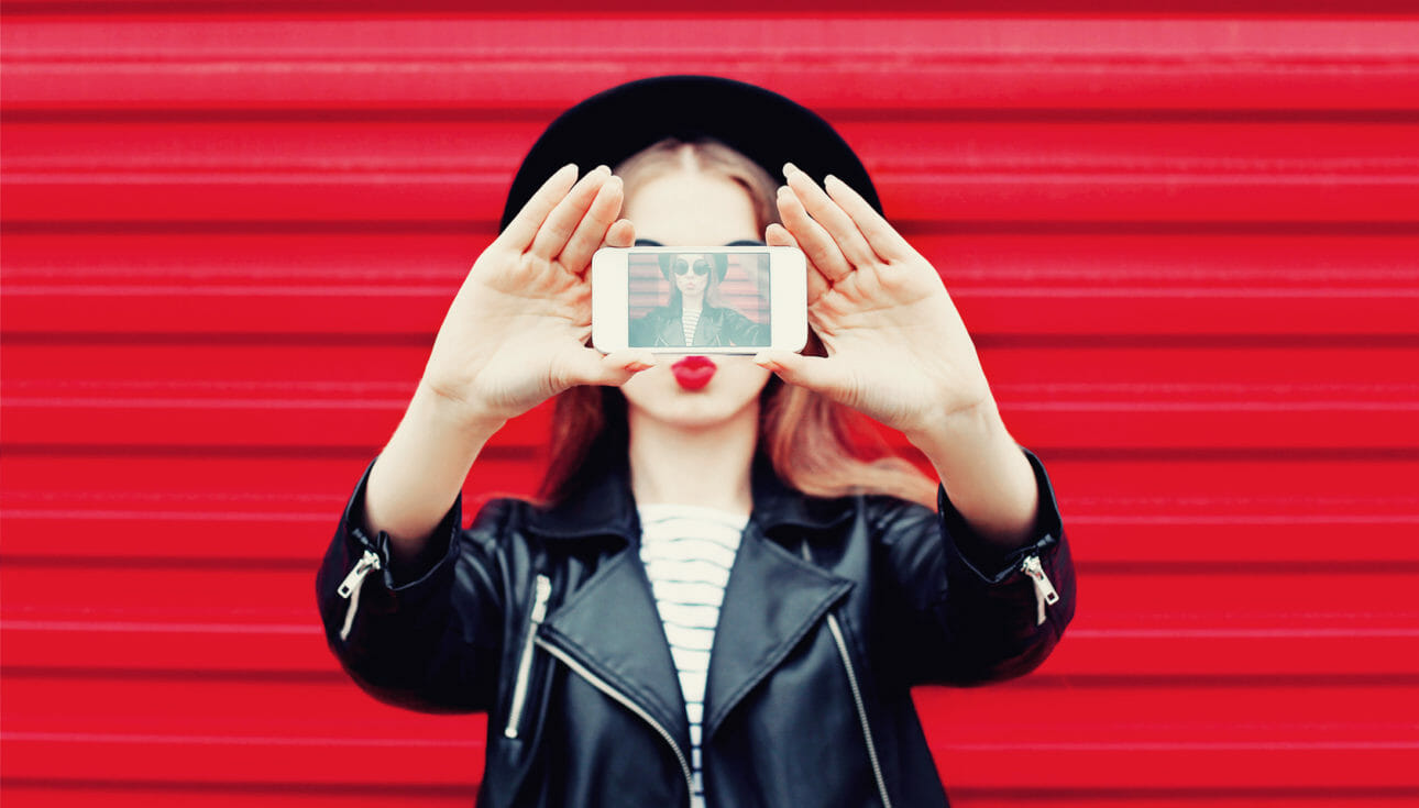 A female influencer holding her phone taking an selfie for social media.