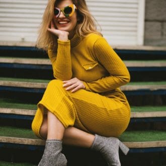 Woman in yellow dress sitting on stairs with colorful sunglasses on.