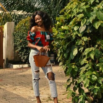 Woman in a flowy top and jeans posing in front of her house.