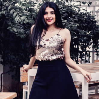 Woman posing in sequin top and black skirt with gold hoop earrings on.